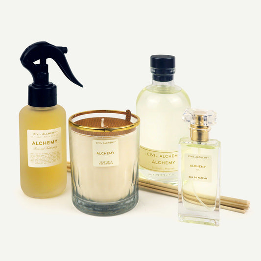 Collection of Alchemy products including a spray bottle, candle, and perfume on a white background