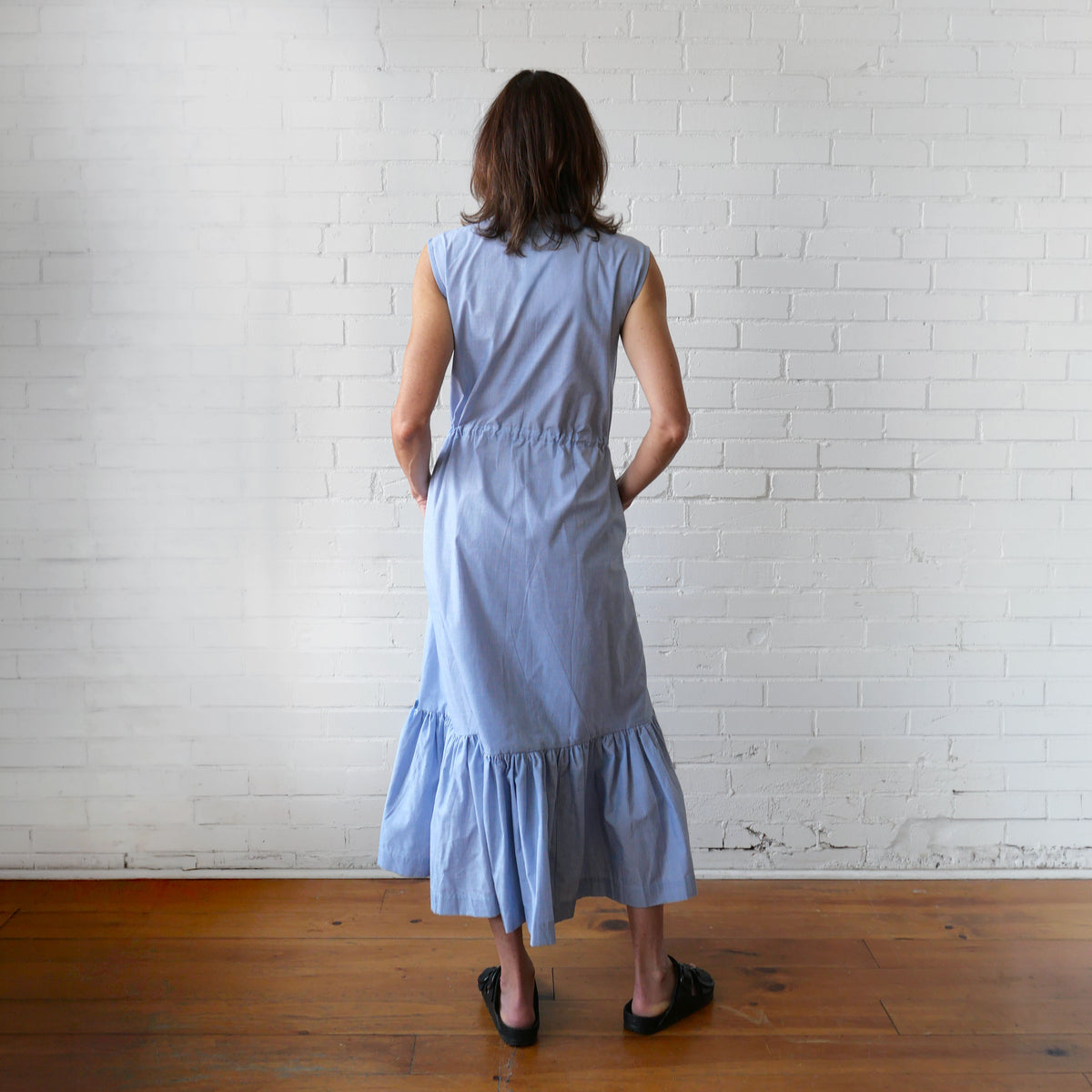 Woman wearing a light blue dress standing against a white brick wall.