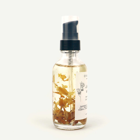 Clear glass bottle with a black spray top containing dried herbs on a white background