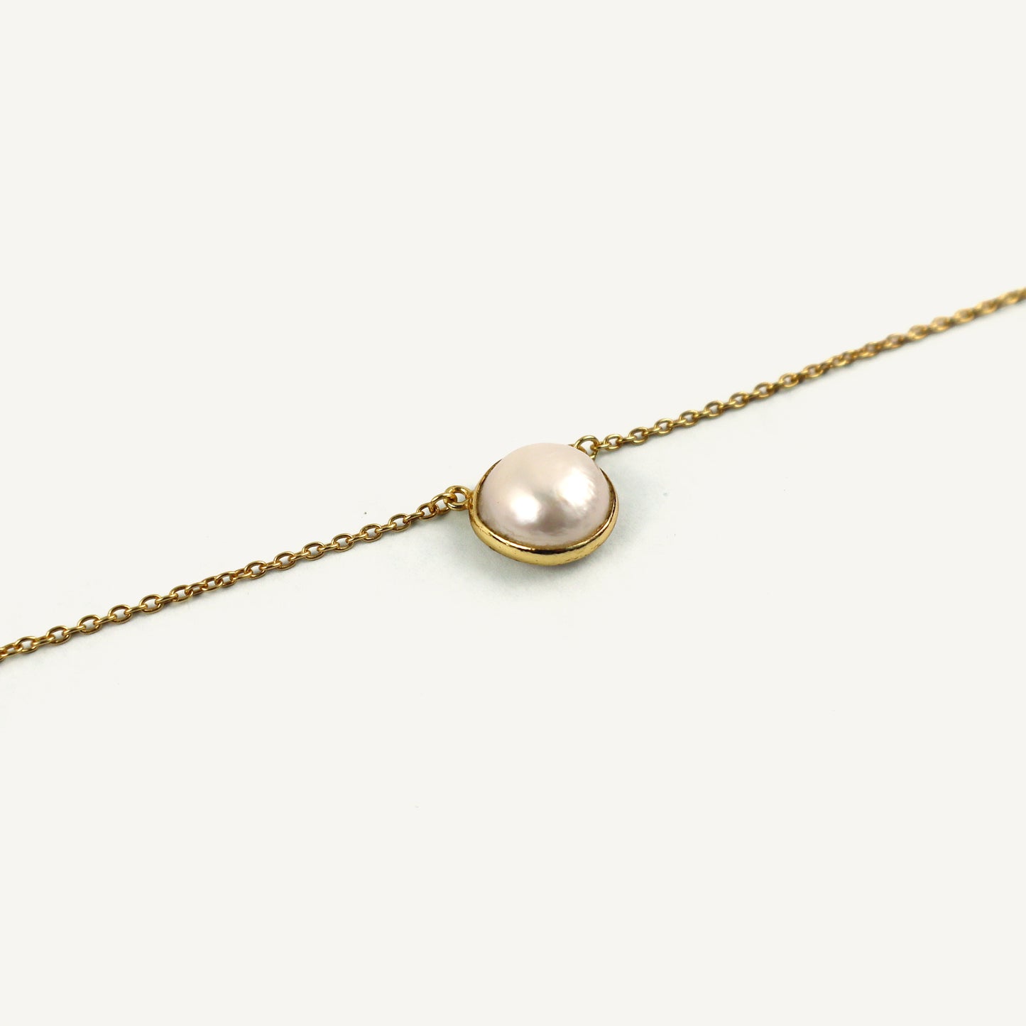 Gold chain necklace with a single pearl pendant on a white background