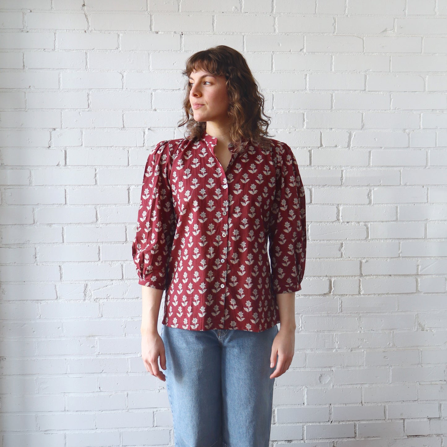 Person wearing a red floral blouse against a white brick wall