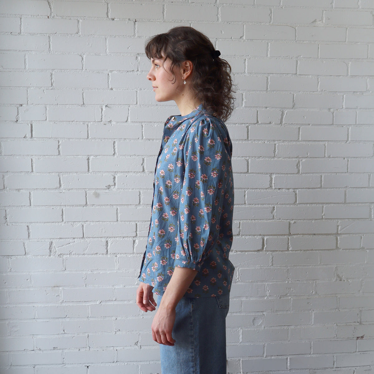 Woman wearing a blue floral blouse against a white brick wall