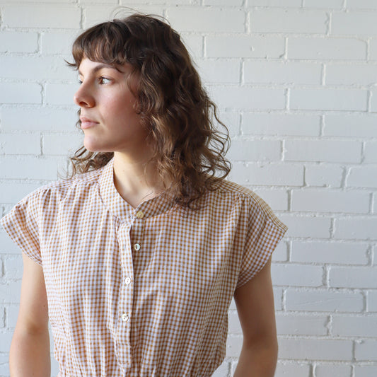 Woman wearing a checkered shirt against a white brick wall