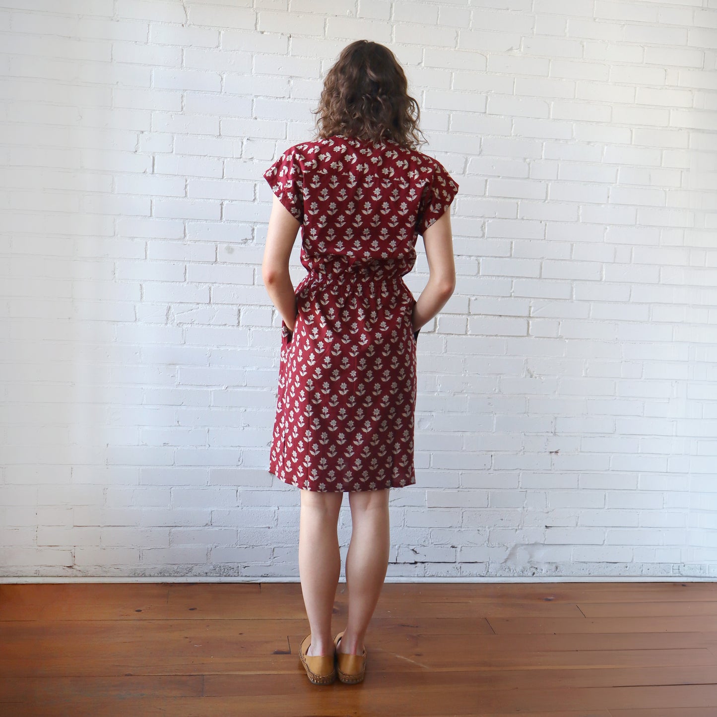 Woman wearing a red patterned dress against a white brick wall.