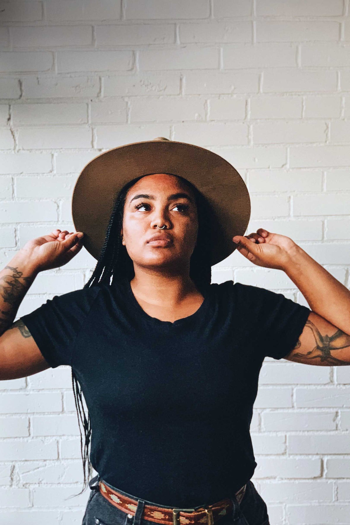 Woman wearing a wide-brimmed hat against a white brick wall