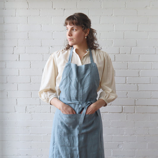 Woman wearing a blue apron against a white brick wall