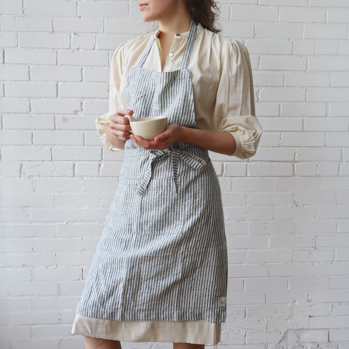 Person wearing a striped apron holding a cup against a white brick wall