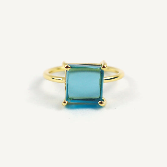Gold ring with a square-cut blue gemstone on a white background