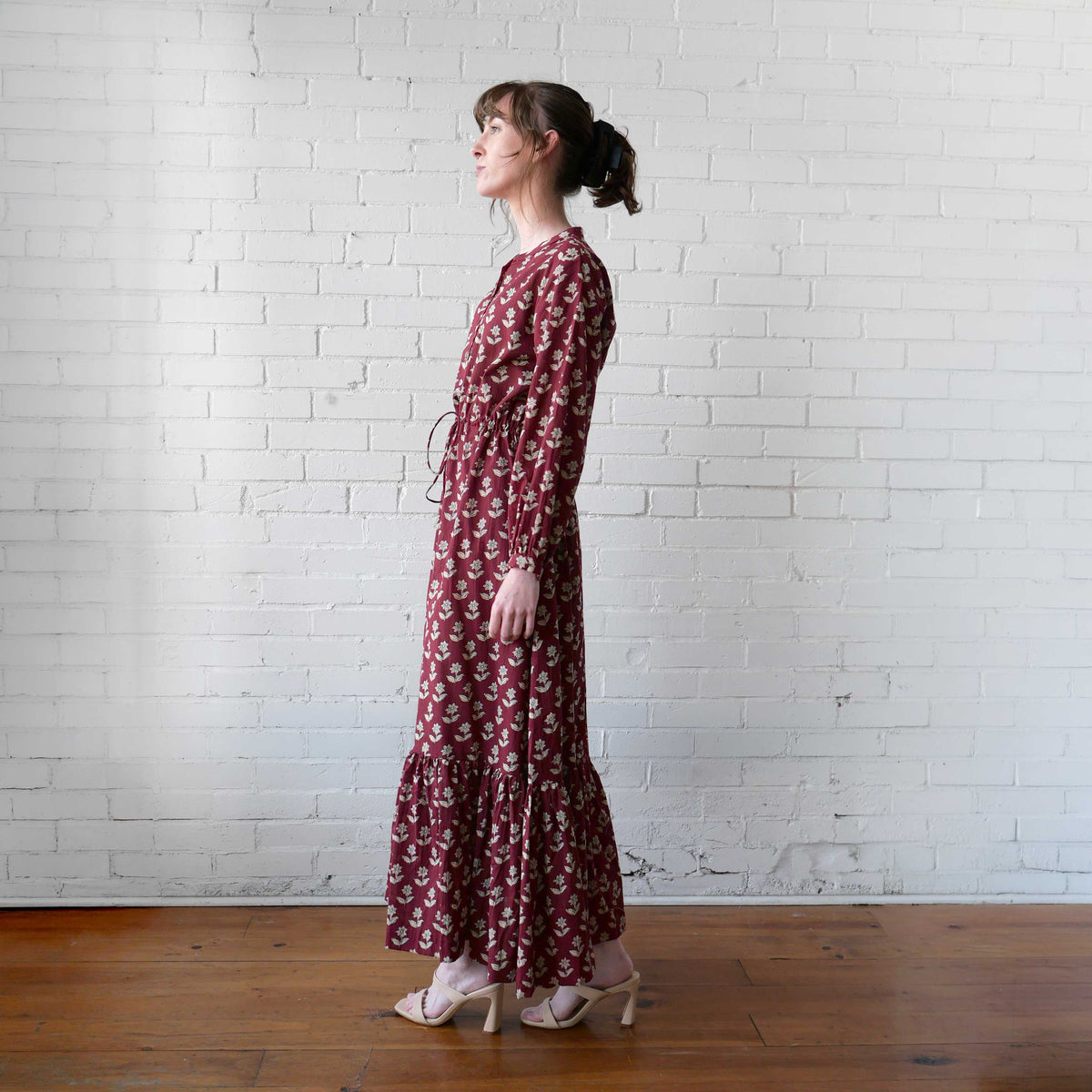 Woman wearing a long floral dress standing against a white brick wall.