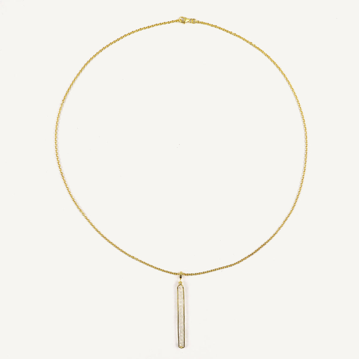 Gold necklace with a vertical bar pendant on a light beige background