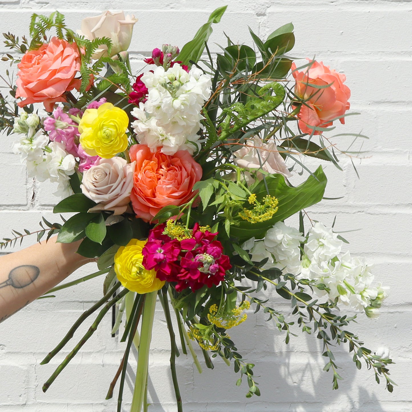 Bouquet of colorful flowers held by a person against a white brick wall.