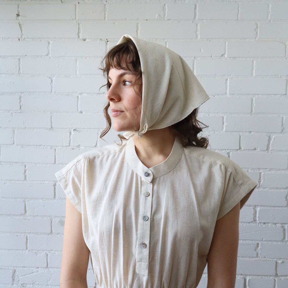 Woman wearing a beige bonnet against a white brick wall