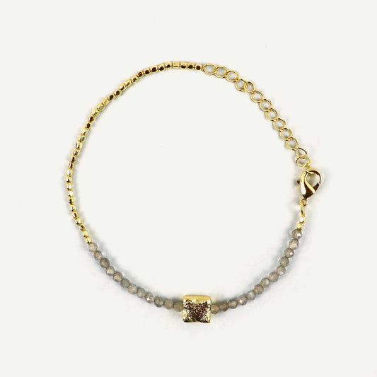 Gold bracelet with a square pendant on a light gray background