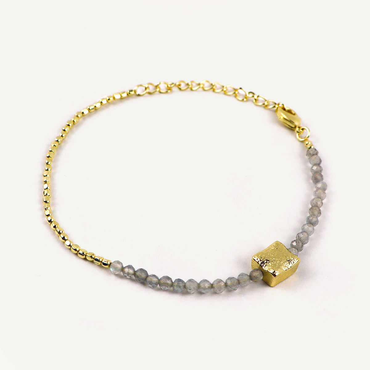 Gold bracelet with gray beads and a gold cube charm on a white background