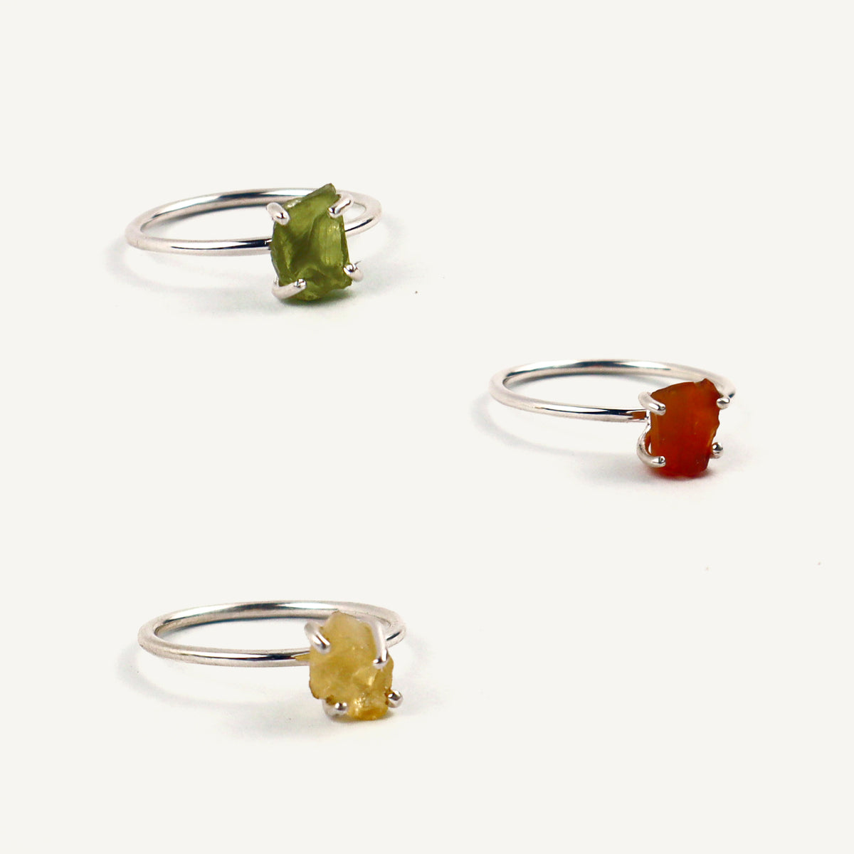 Three silver rings with different colored gemstones on a white background