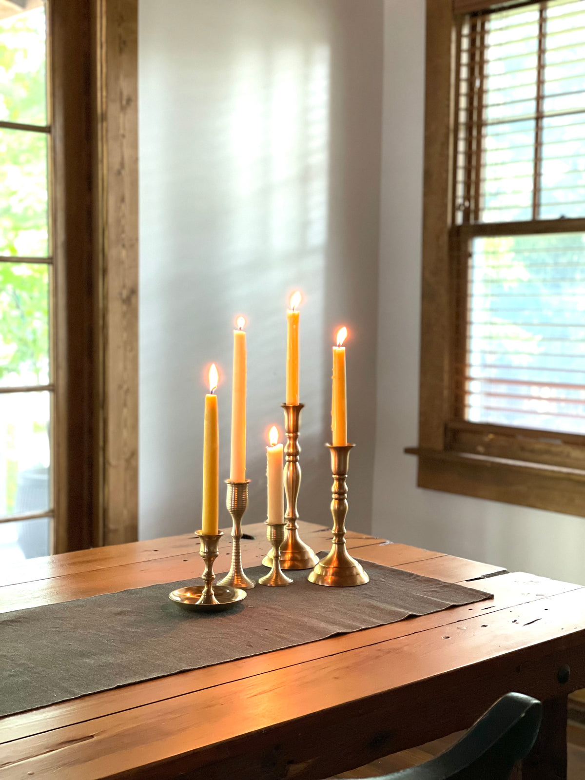 Candlelit scene on a wooden table with brass candlesticks and a window in the background.