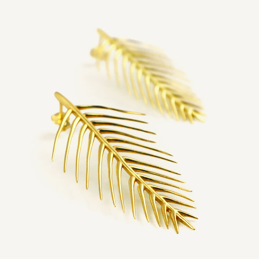 Gold leaf-shaped earrings on a light beige background