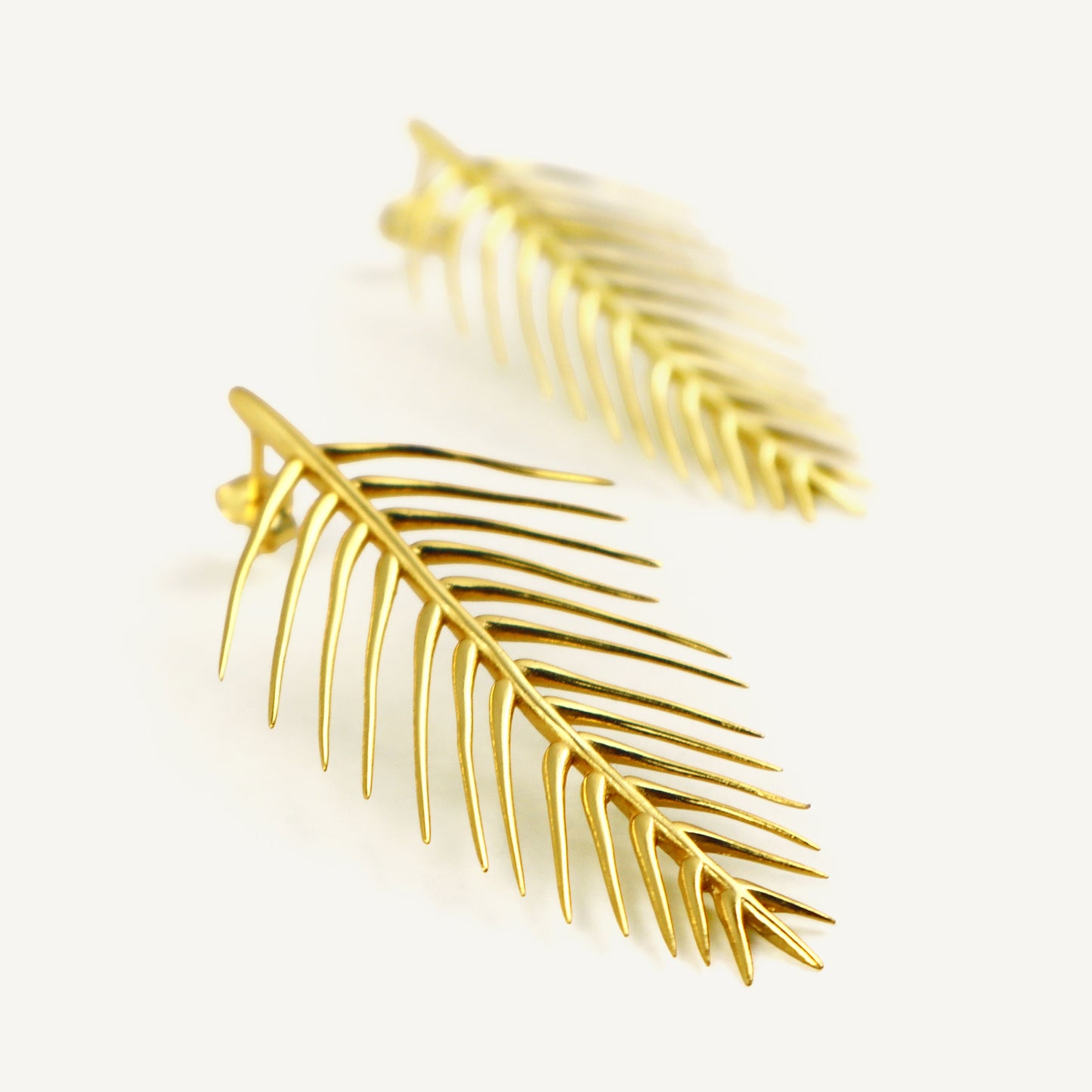 Gold leaf-shaped earrings on a light beige background