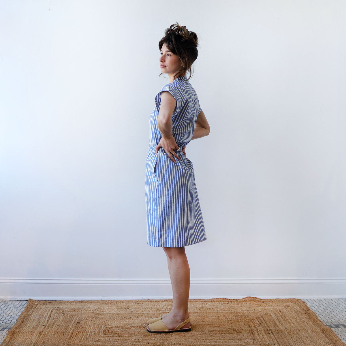 Woman wearing a blue and white striped dress standing against a plain white wall.