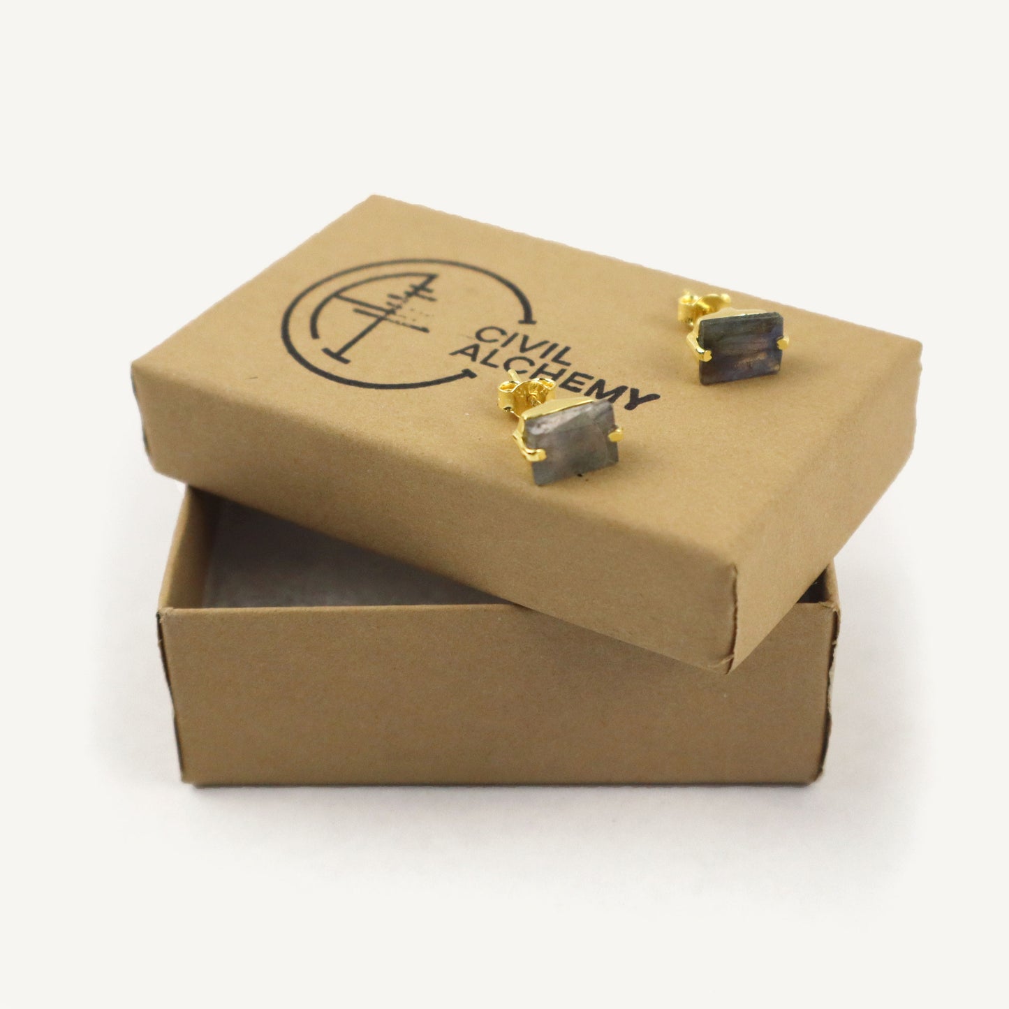 Open cardboard box with earrings on a white background, featuring 'Civil Alchemy' branding.