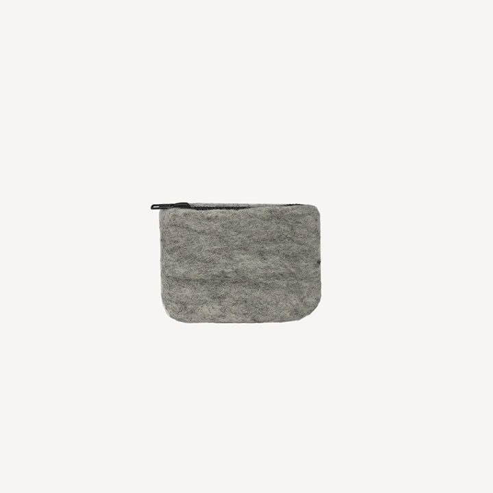 A solid black wool coin pouch with a brass zipper, hand-felted by artisans in Nepal.
