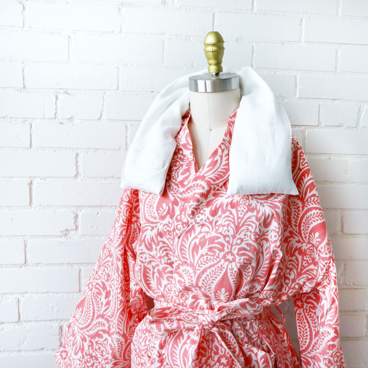 Red and white patterned robe with therapy wrap on a mannequin against a white brick wall.
