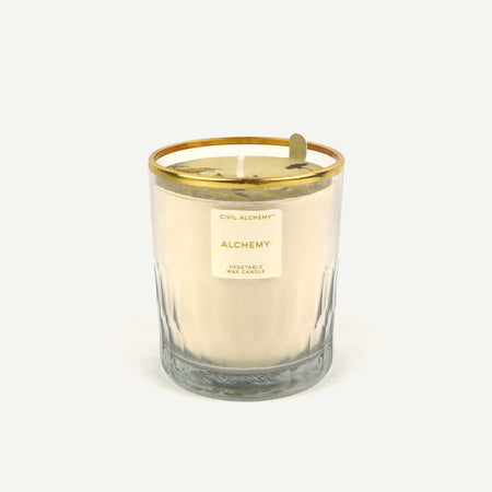 Candle with gold lid and 'Alchemy' label on a white background