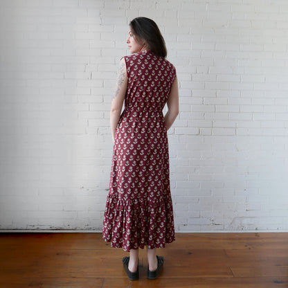Woman wearing a red floral dress standing against a white brick wall.