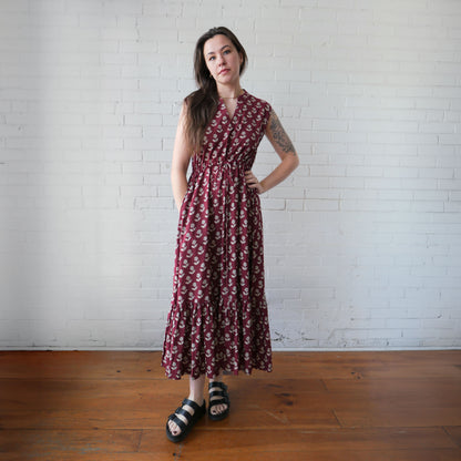 Woman wearing a patterned dress standing against a white brick wall.