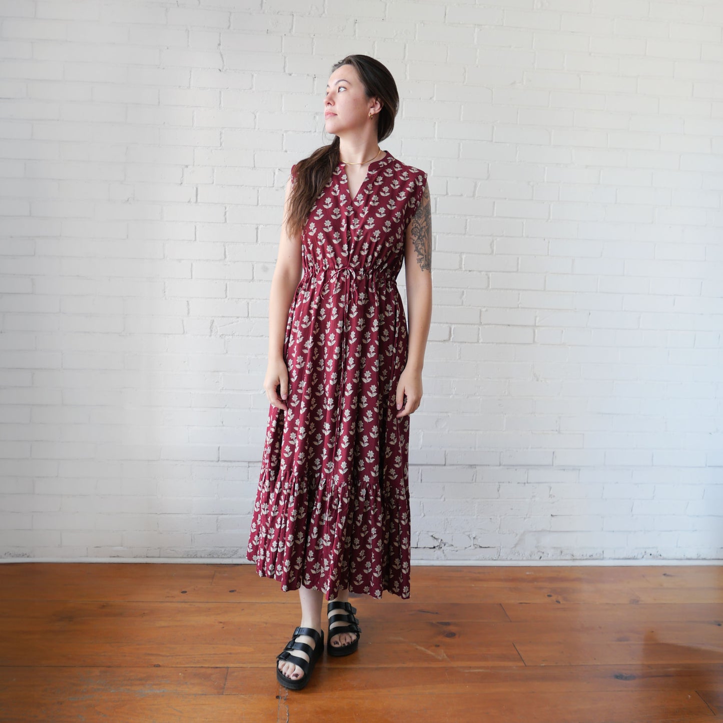 Woman wearing a red floral dress standing against a white brick wall.
