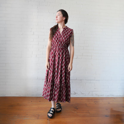 Woman wearing a red floral dress standing against a white brick wall.