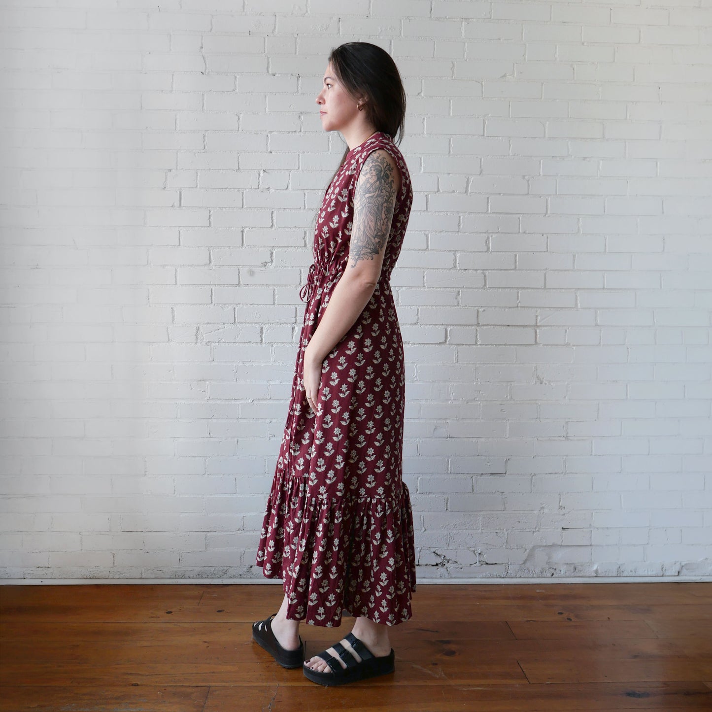 Woman in a red floral dress standing against a white brick wall.
