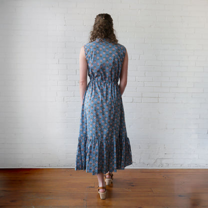 Woman wearing a blue floral dress standing in front of a white brick wall.