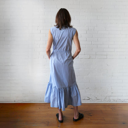 Woman wearing a light blue dress standing against a white brick wall.