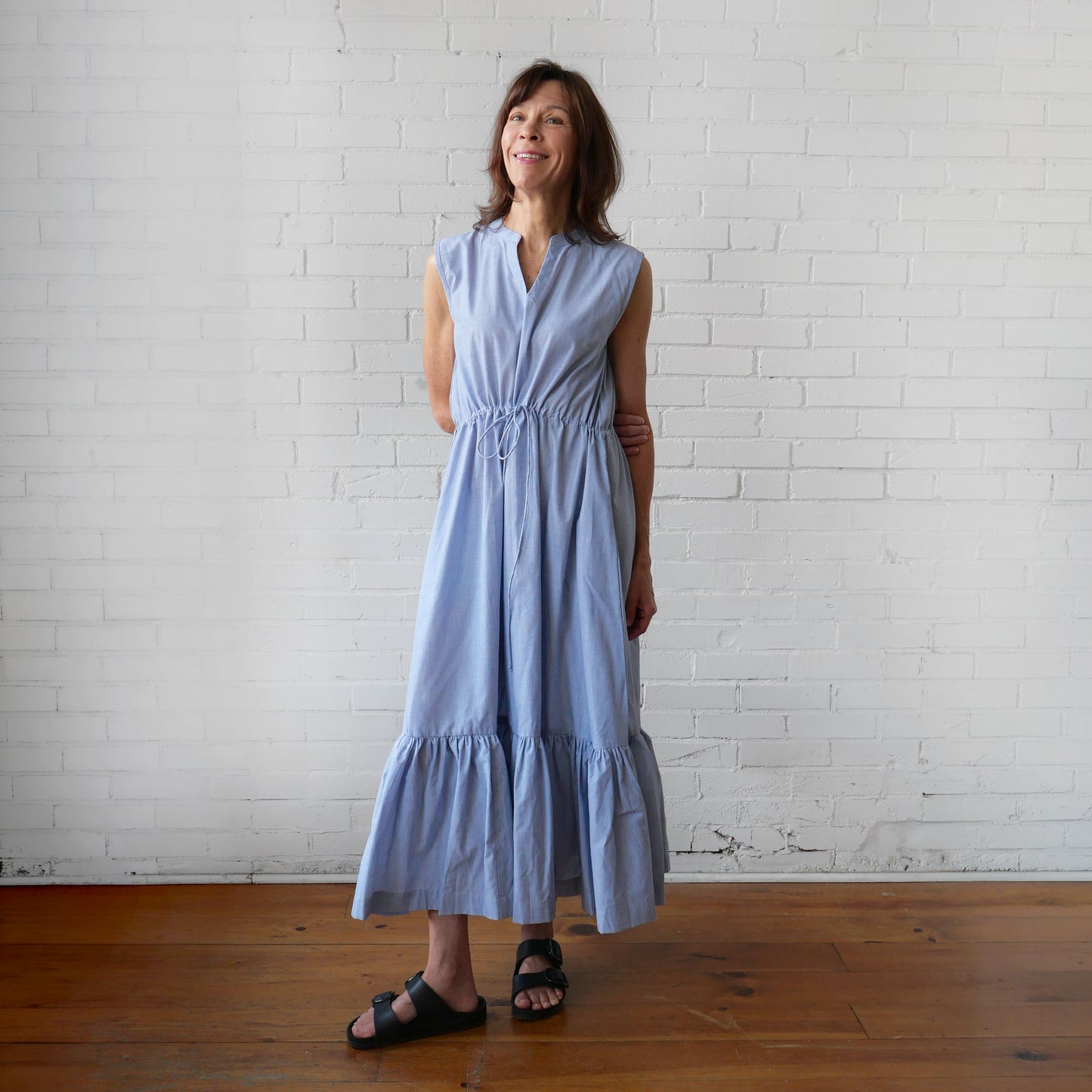 Woman wearing a light blue dress standing against a white brick wall.