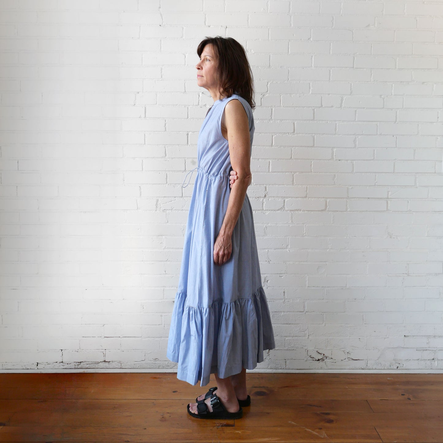 Woman wearing a light blue dress standing against a white brick wall.