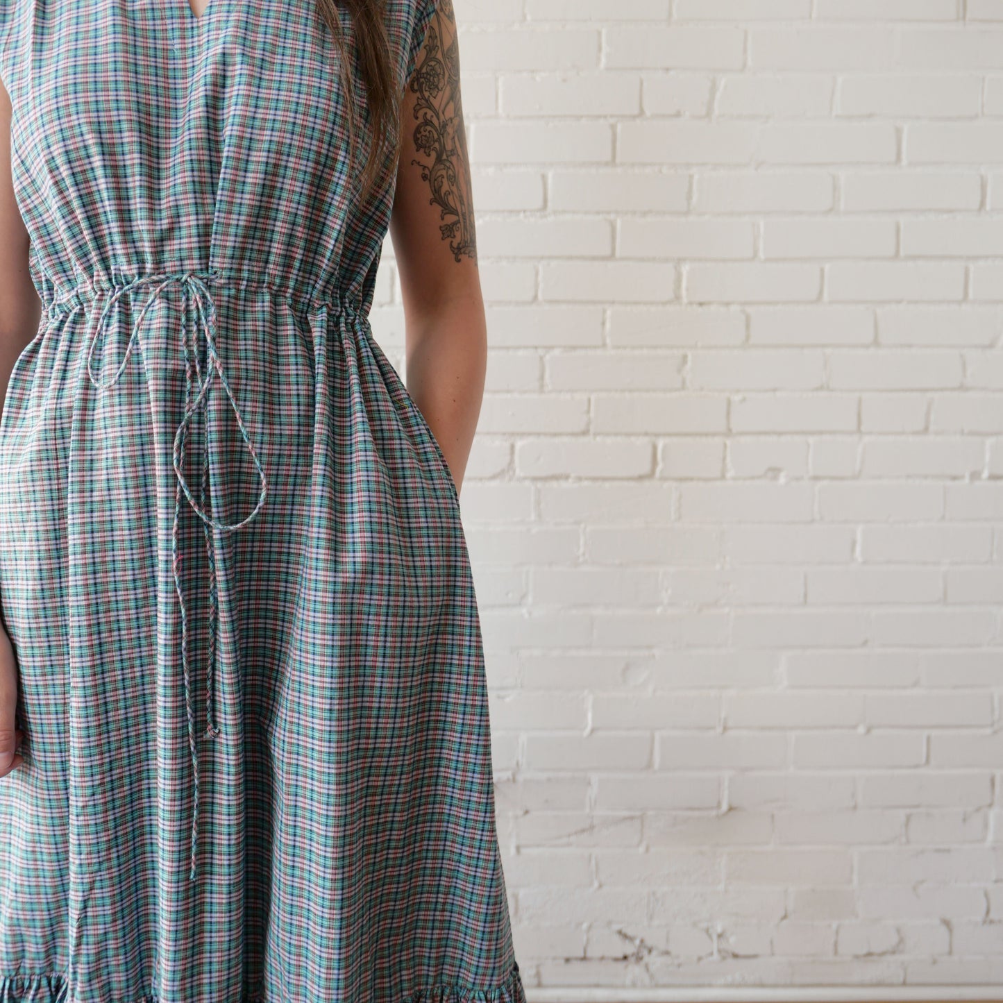 Person wearing a plaid dress against a white brick wall