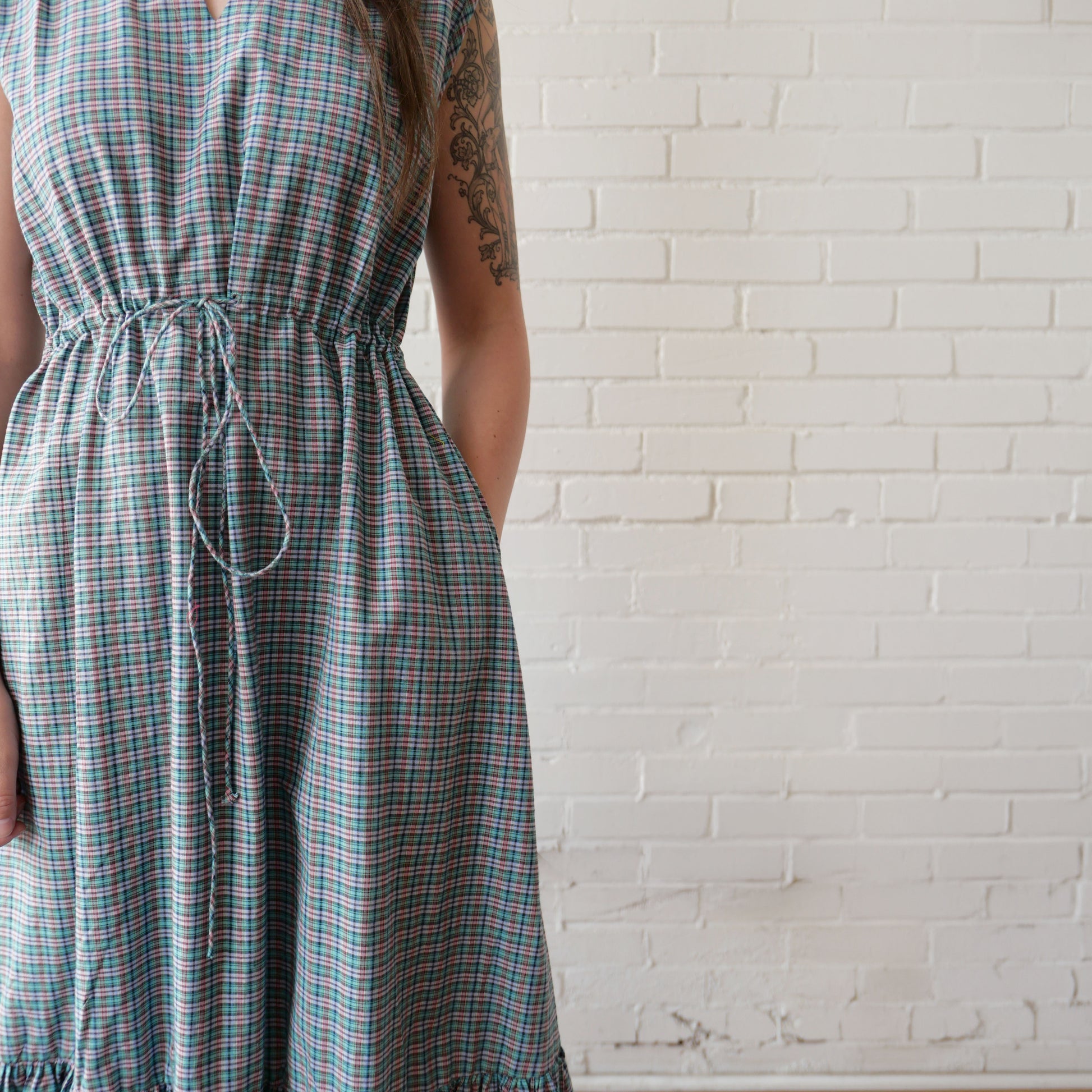 Person wearing a plaid dress against a white brick wall