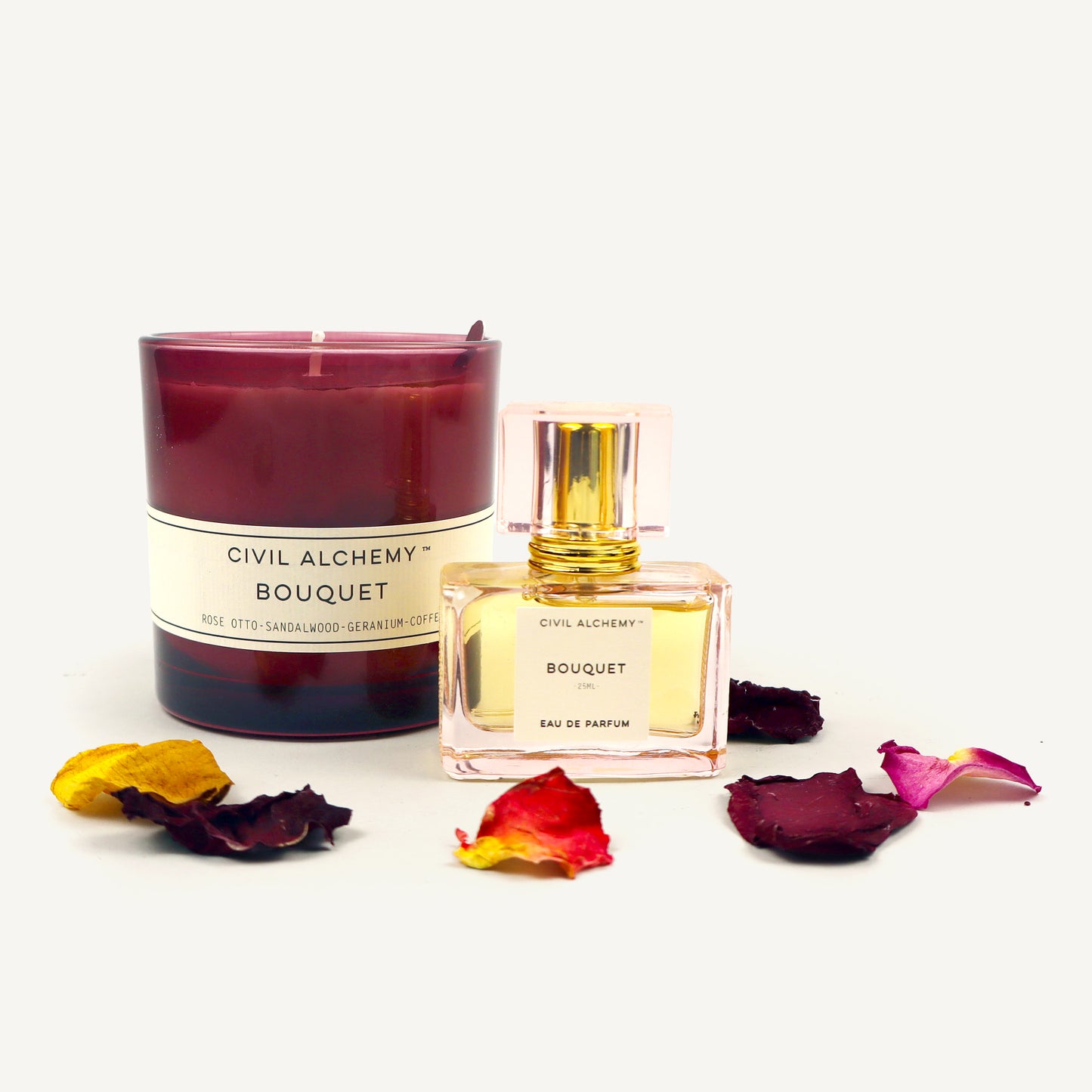 Candle and perfume bottle labeled 'Civil Alchemy Bouquet' with flowers on a white background