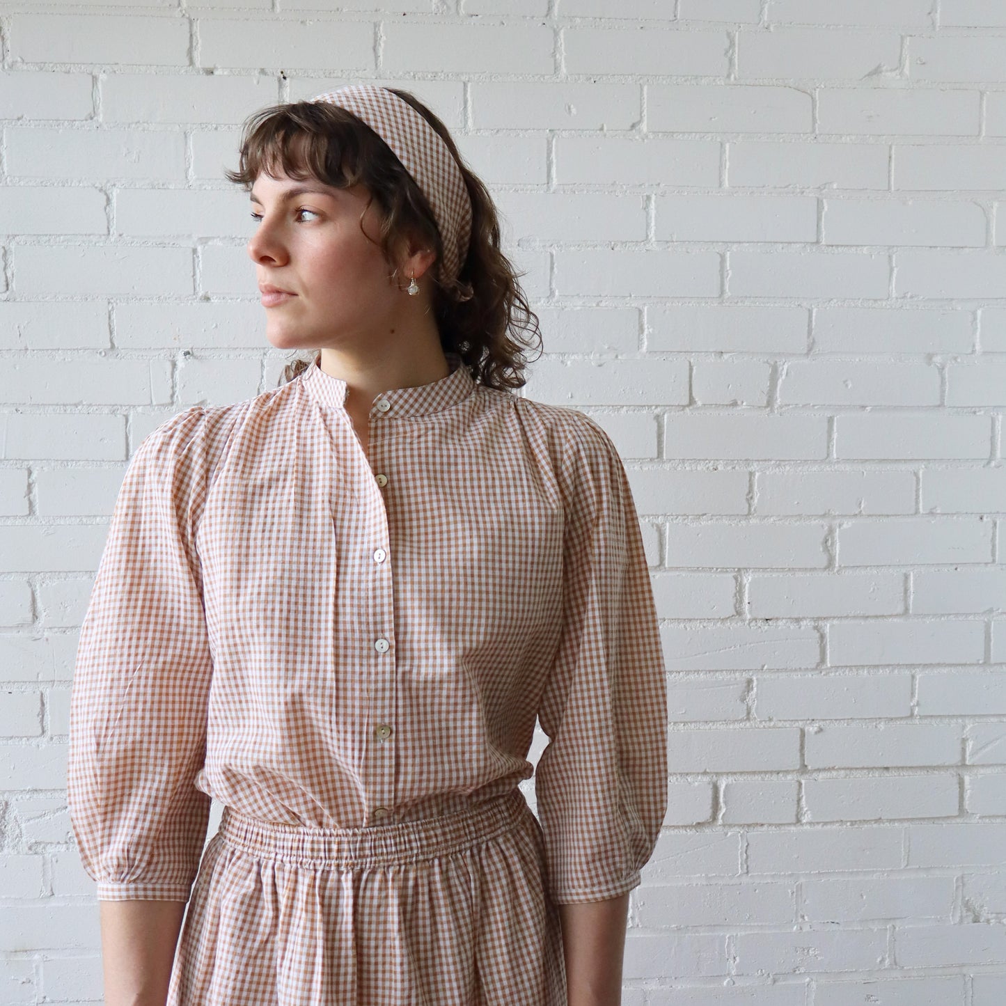 Woman wearing a checkered dress standing against a white brick wall
