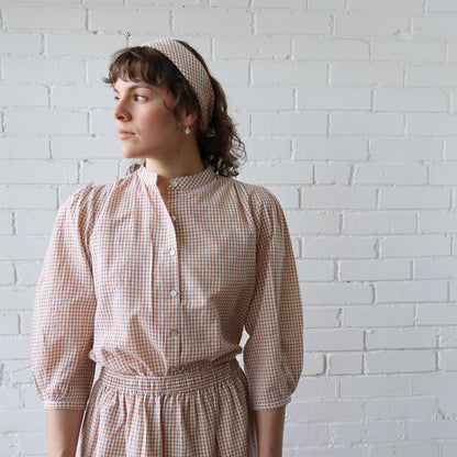 Woman wearing a checkered dress standing against a white brick wall