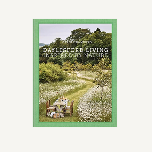 Book cover of 'Daylesford Living Inspired by Nature' with a green border and image of a person sitting at a table in a garden.