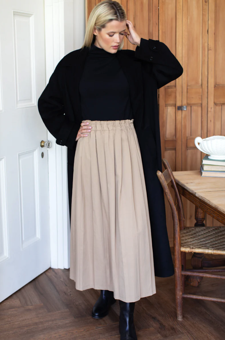 Woman wearing a black top and beige skirt indoors.