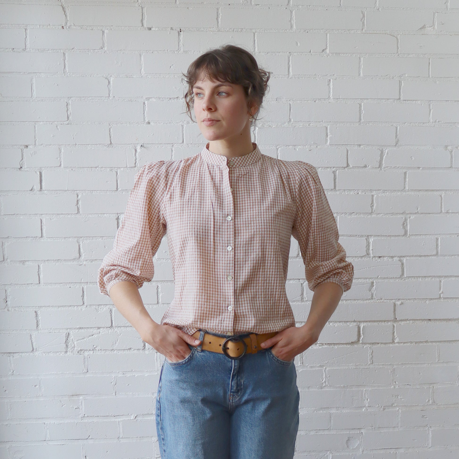 Woman wearing a checkered shirt and jeans against a white brick wall
