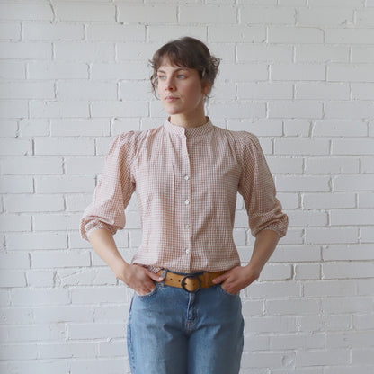 Woman wearing a checkered shirt and jeans against a white brick wall