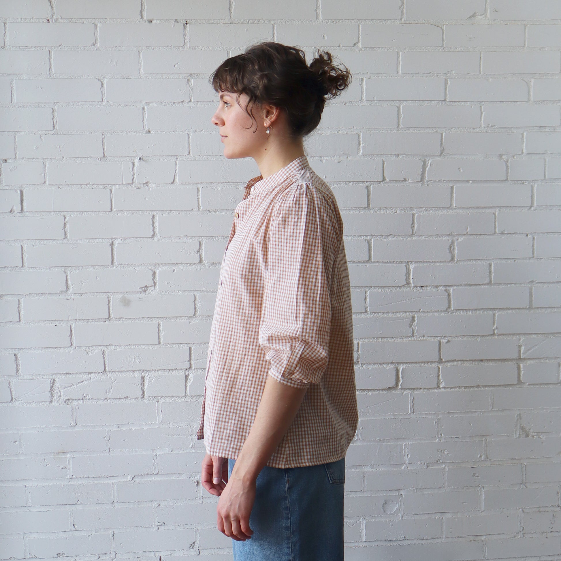 Woman wearing a checkered shirt against a white brick wall