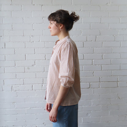 Woman wearing a checkered shirt against a white brick wall