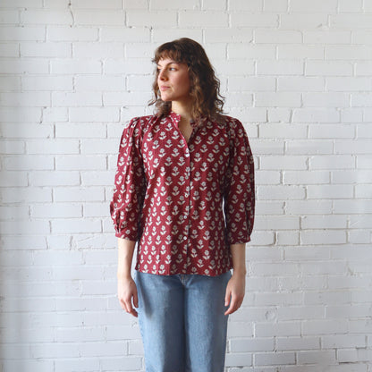 Person wearing a red floral blouse against a white brick wall