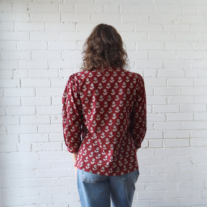 Person wearing a red patterned shirt and blue jeans against a white brick wall.