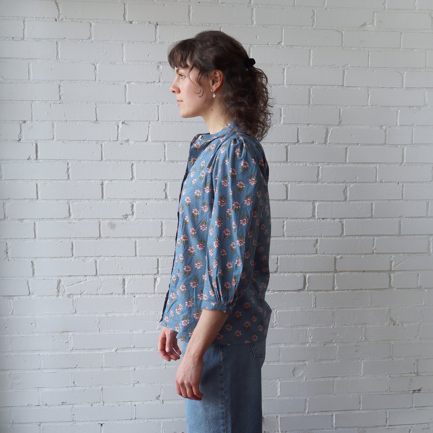 Woman wearing a blue floral blouse against a white brick wall